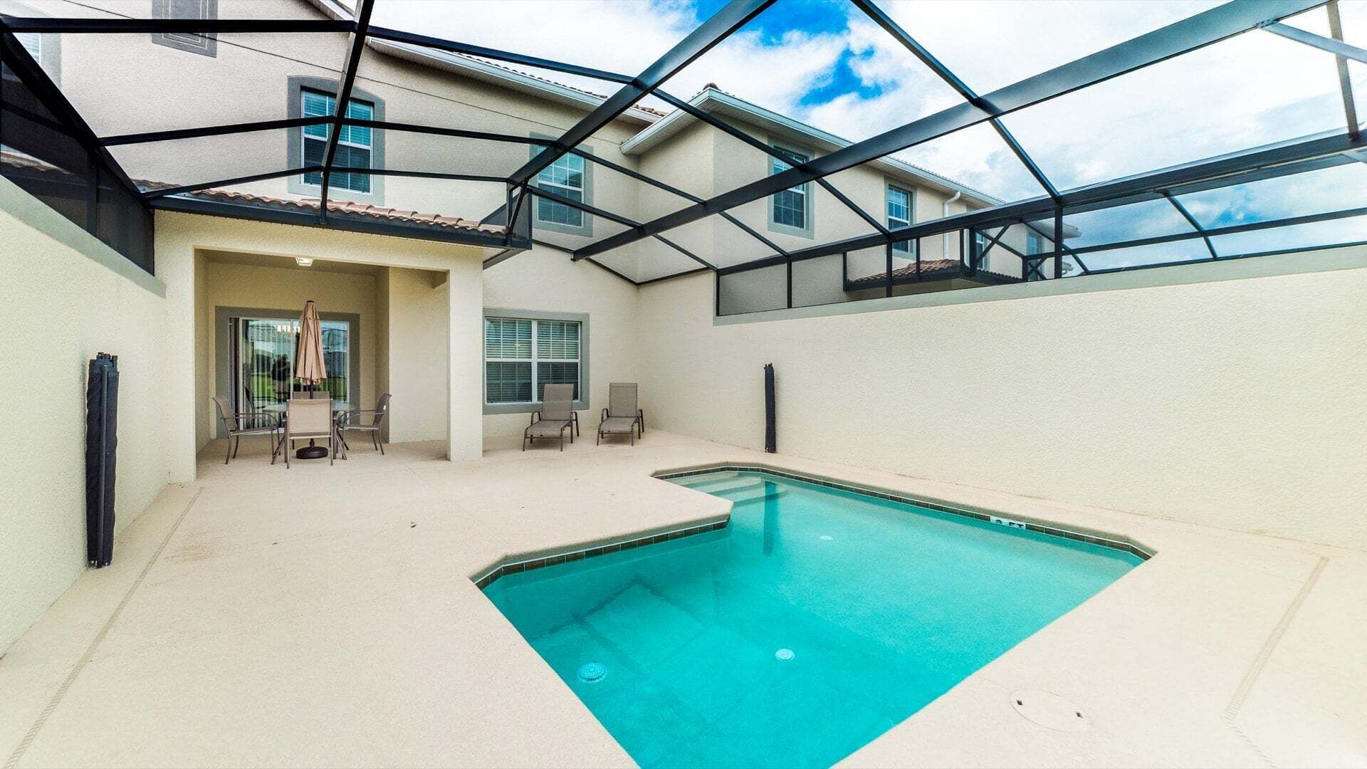 An indoor swimming pool with a glass ceiling, a patio area with chairs, and a view of a building.