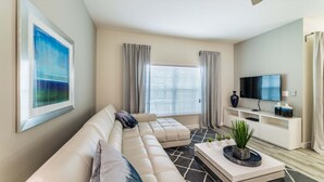 A modern living room with a sectional sofa, a flat-screen TV, a coffee table with plants, and a painting on the wall. - Peq3141 (Kissimmee)