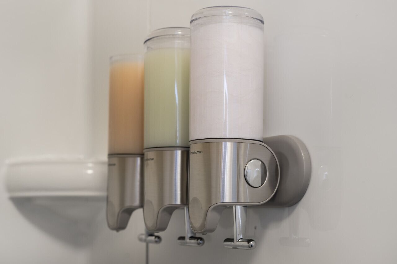 A bathroom with three soap dispensers mounted on a wall.