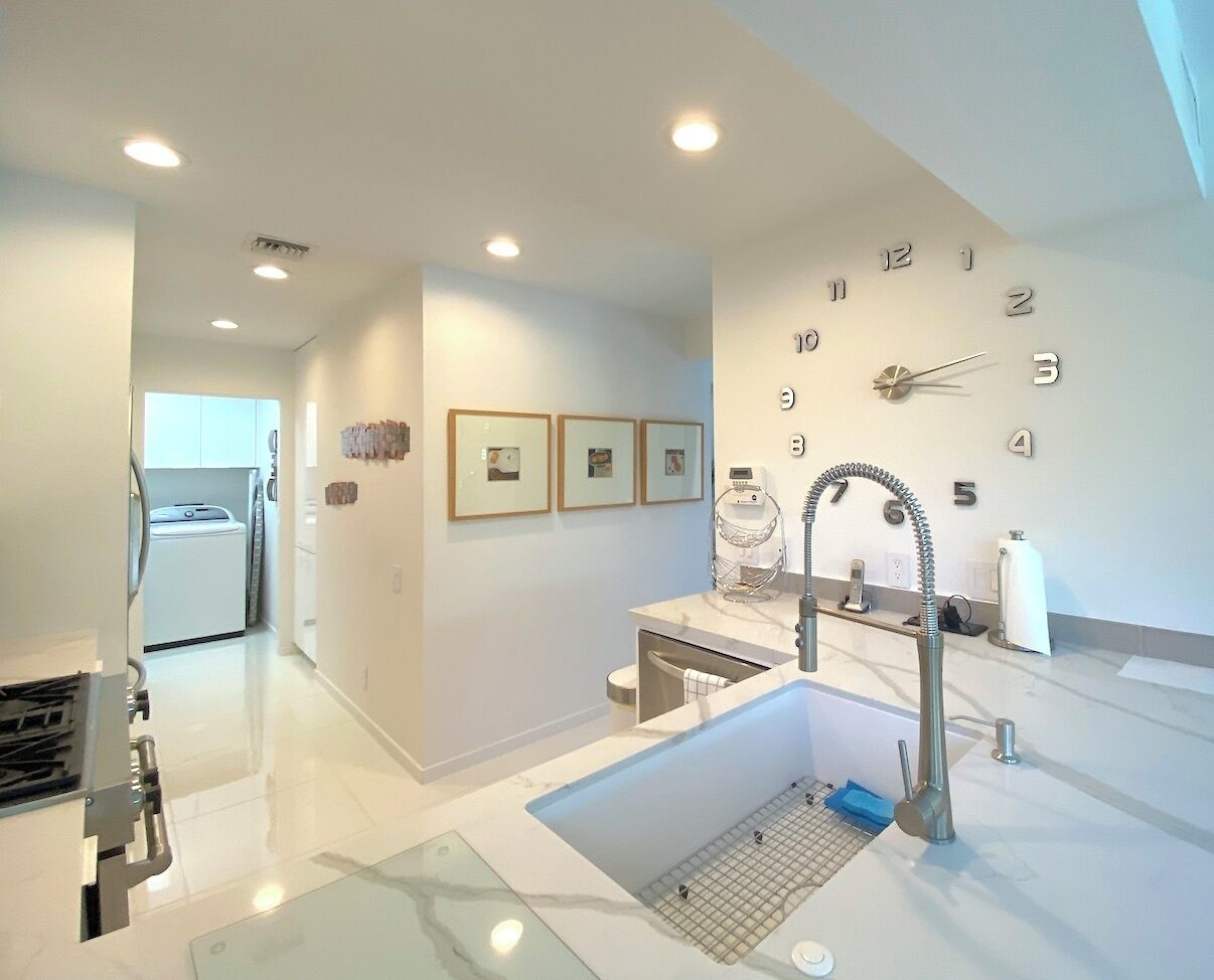 A modern kitchen with a large sink, a dishwasher, and a built-in oven. There are framed pictures on the wall and a clock.