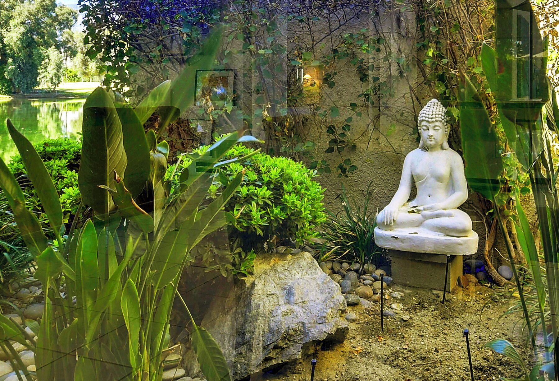 Ein friedlicher Garten mit einer weißen Buddha-Statue, üppigem Grün und einem Steinbau.