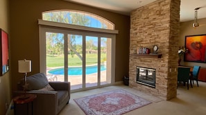 Ein Wohnzimmer mit Kamin, Blick auf einen Pool und einem Essbereich.