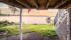 A covered outdoor area with a view of a lake, a wooden deck, and a metal fence.