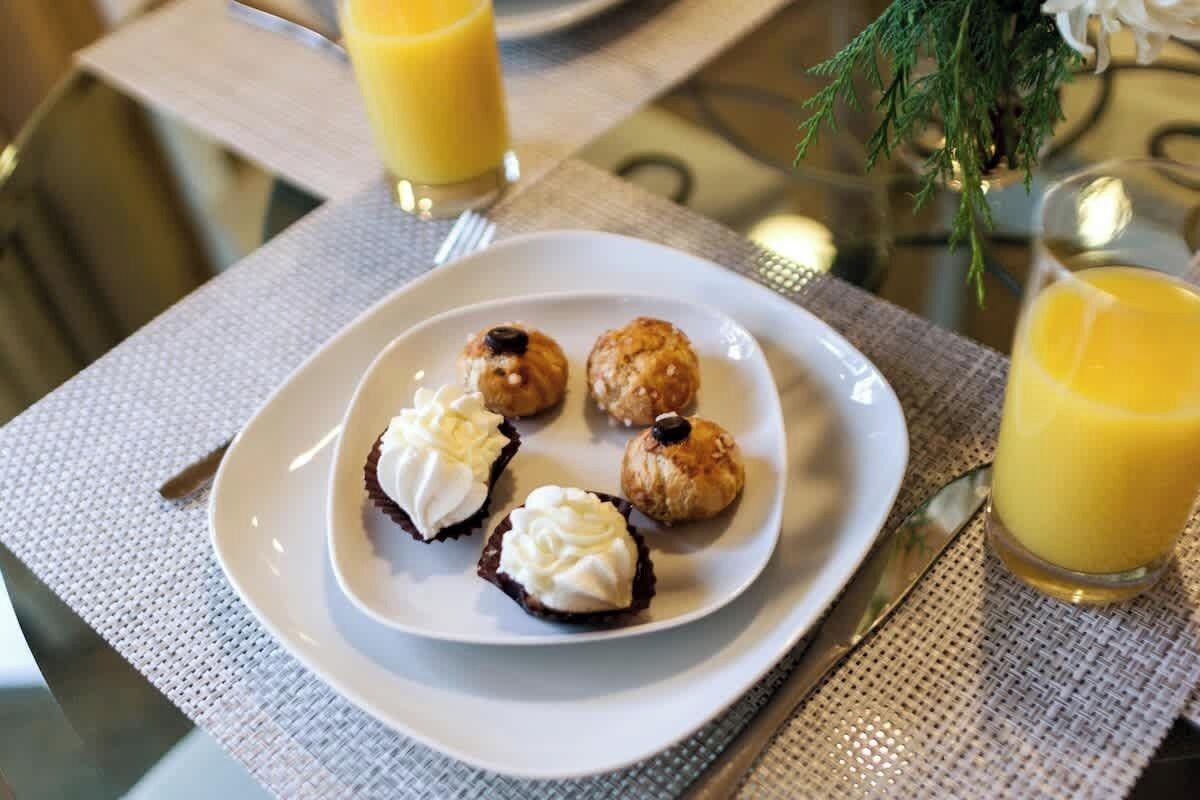 Une table mise pour le petit-déjeuner, avec une assiette de viennoiseries, deux verres de jus d’orange et une fourchette.