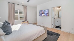 Ein modernes Schlafzimmer mit Bett, Deckenventilator, Fernseher und einem durchgehenden Türrahmen sichtbaren Badezimmer.