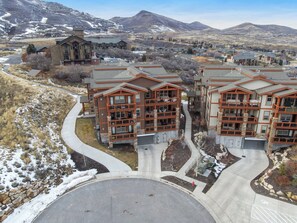A multi-story building with a stone facade and large windows, surrounded by a landscaped area with a curved driveway and a snow-covered landscape in the background.