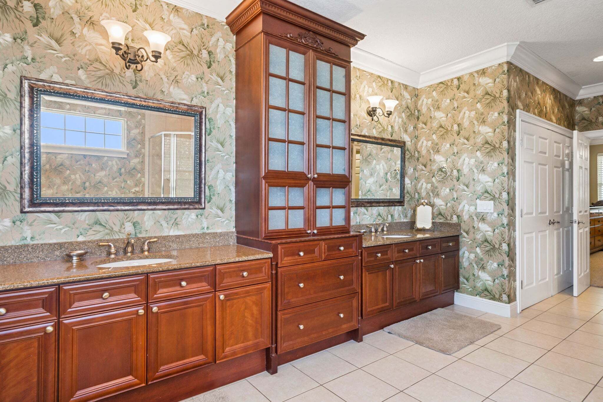 Un baño con un mueble de tocador de madera grande, dos lavabos, un espejo y un armario con puertas de cristal.