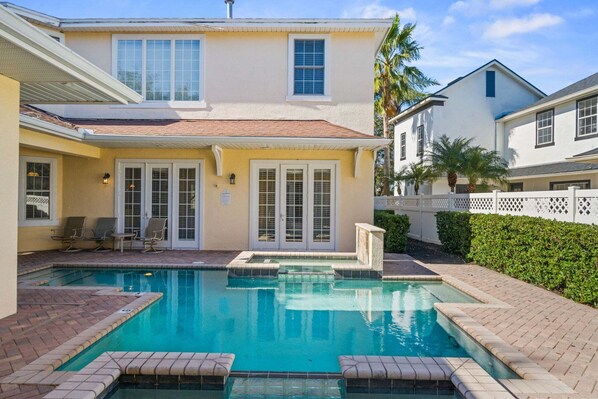 Une maison à deux étages avec une piscine, un patio couvert et une clôture blanche.