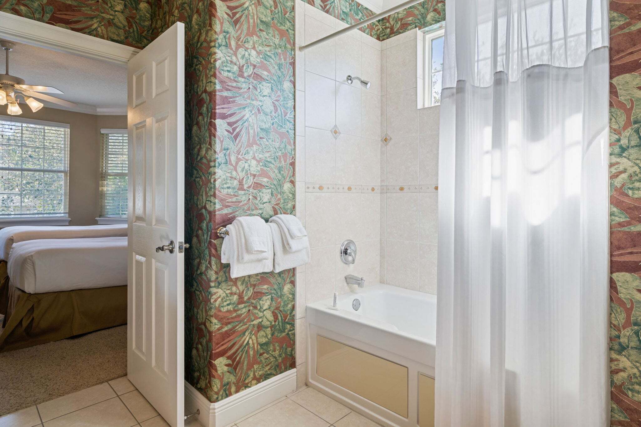 A bathroom with a shower, a bathtub, and a door leading to a bedroom.
