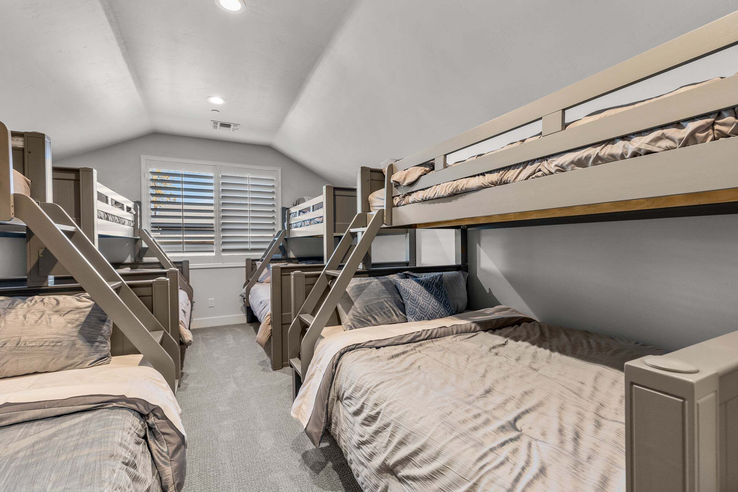 A dormitory room with bunk beds, a staircase, and a window with blinds.