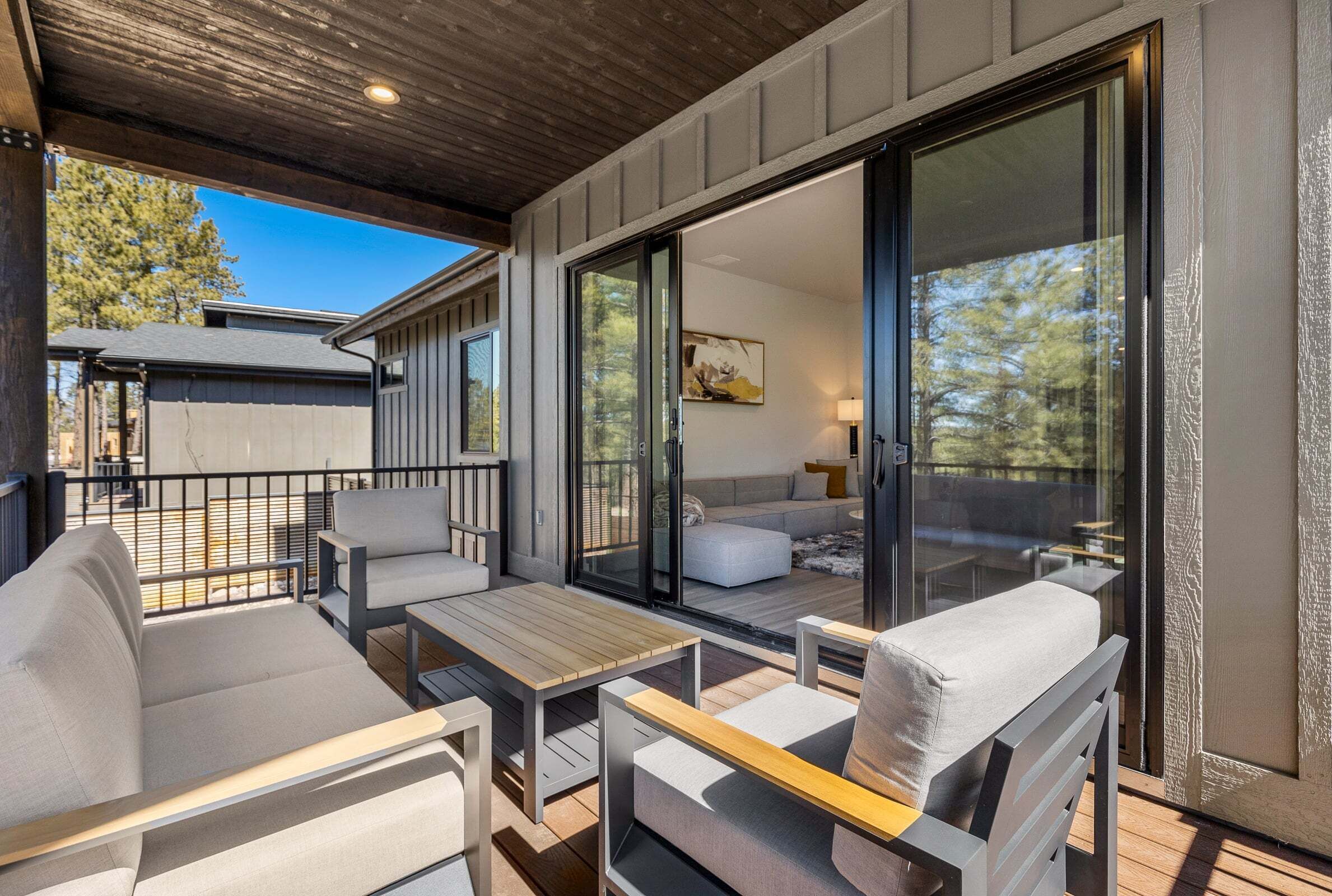 A modern outdoor living area with a wooden ceiling, sliding glass doors leading to a balcony, and a sofa set.