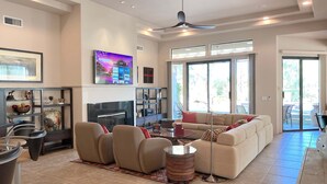 A spacious living room with a large flat-screen TV, comfortable seating, and a ceiling fan. - Double Eagle (Rancho Mirage)