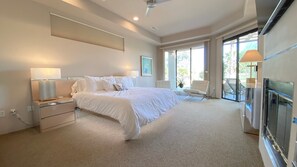 A bedroom with a large bed, bedside lamps, a chair, a fireplace, and a view of the outdoors. - Double Eagle (Rancho Mirage)
