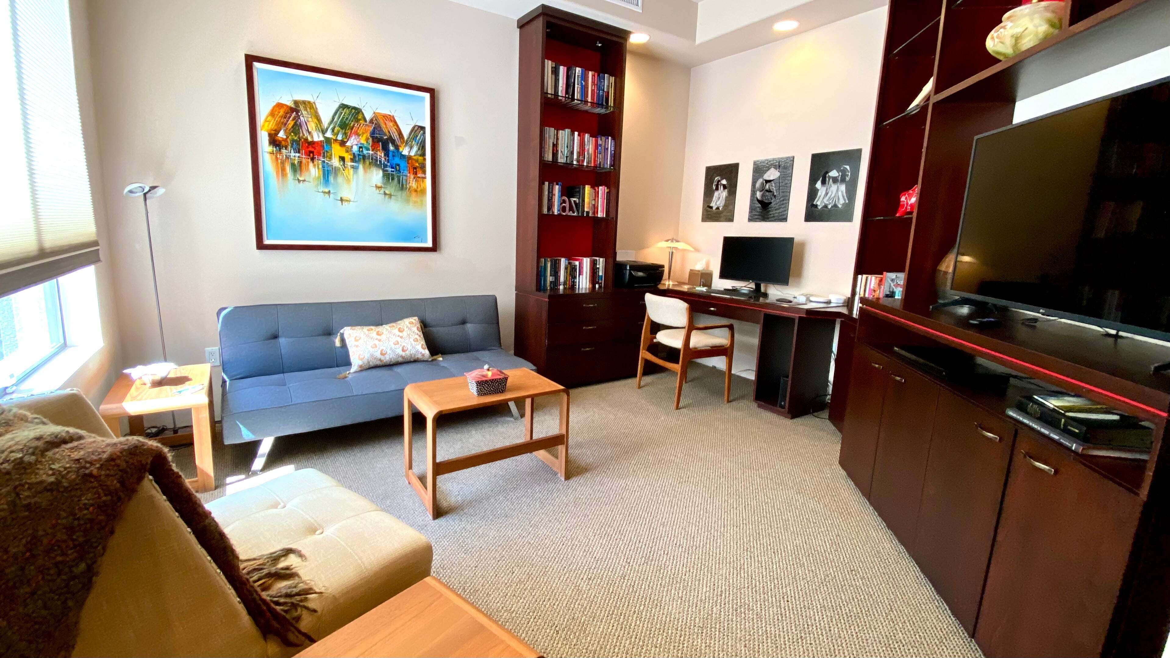 A living room with a sofa, a coffee table, a bookshelf, a desk with a computer, and a TV.