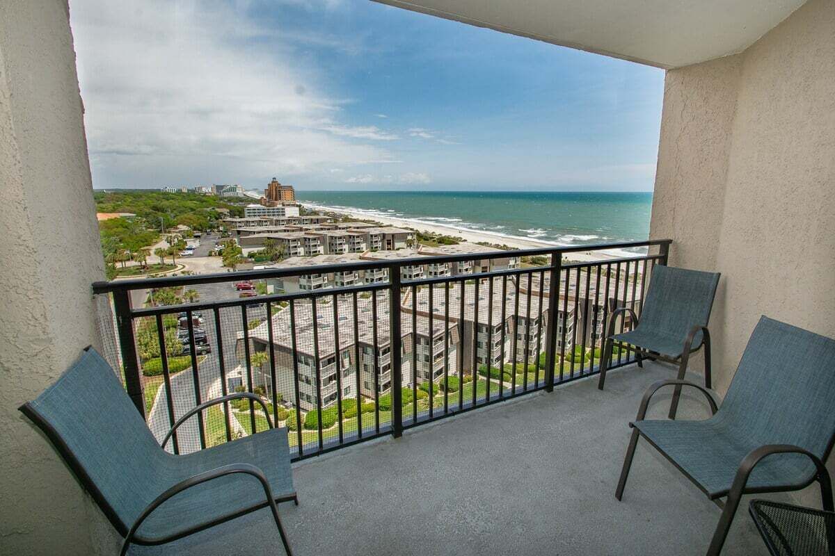 Een balkon met twee stoelen, uitzicht op het strand en gebouwen op de achtergrond.