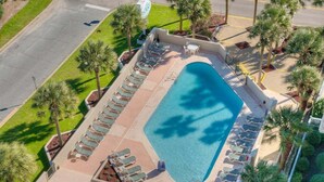 Eine Vogelperspektive zeigt ein Hotel mit einem Swimmingpool, umgeben von Liegestühlen und Palmen.