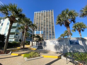 Ein hohes Gebäude mit Balkonen, umgeben von Palmen und einem Schild mit der Aufschrift 'Ocean Forest Plaza'.