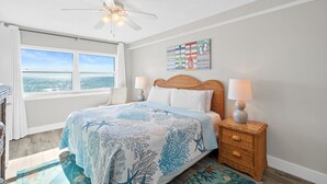 Ein Schlafzimmer mit einem Bett, zwei Nachttischen, einem Deckenventilator, einem Fenster mit Blick und einer Wanddekoration.
