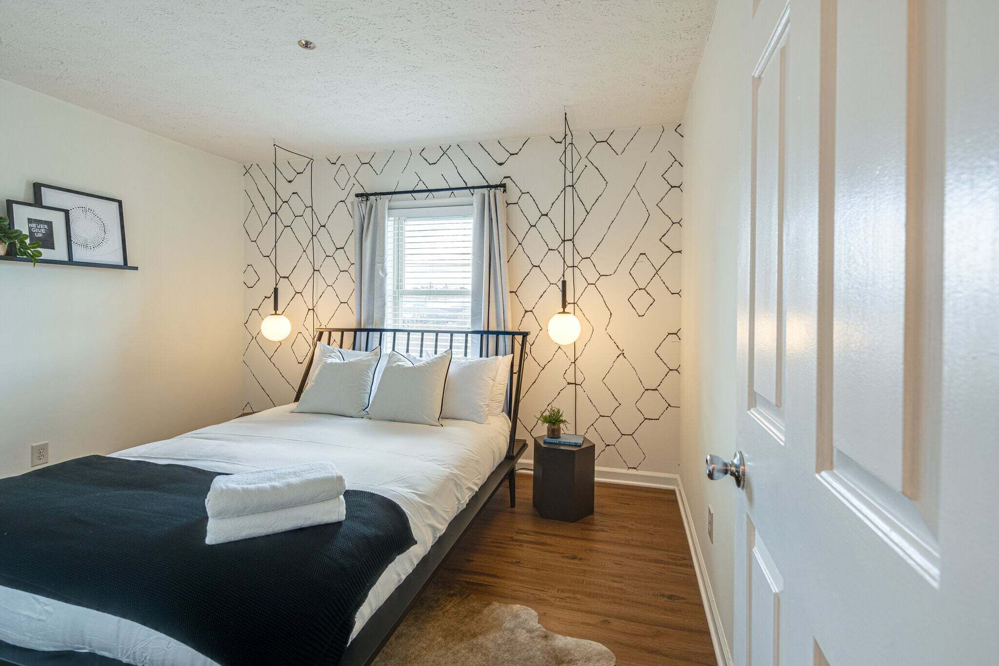 A bedroom with a bed, bedside lamps, a window with curtains, a small plant, and a door.