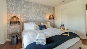 A neatly made bed with a headboard, a bedside table, and a wall with a patterned wallpaper. - Nashville - 1808 State St #208 (Nashville)
