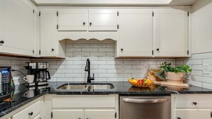 A kitchen with white cabinets, a black countertop, a stainless steel sink, a coffee maker, and a dishwasher. - Nashville - 1808 State St #208 (Nashville)