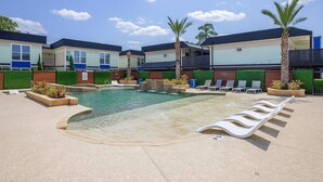 A swimming pool with lounge chairs and palm trees, surrounded by buildings with a modern design. - Kingbed, Resort Style Pool, Gym, Neartheheights (Houston)