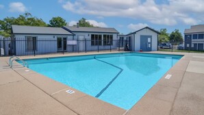 A rectangular swimming pool with a metal ladder on one side, surrounded by a fence and buildings with grey roofs and blue walls. - Kingbed,a+location,a+for Workers, Longstaydiscount (Sherman)