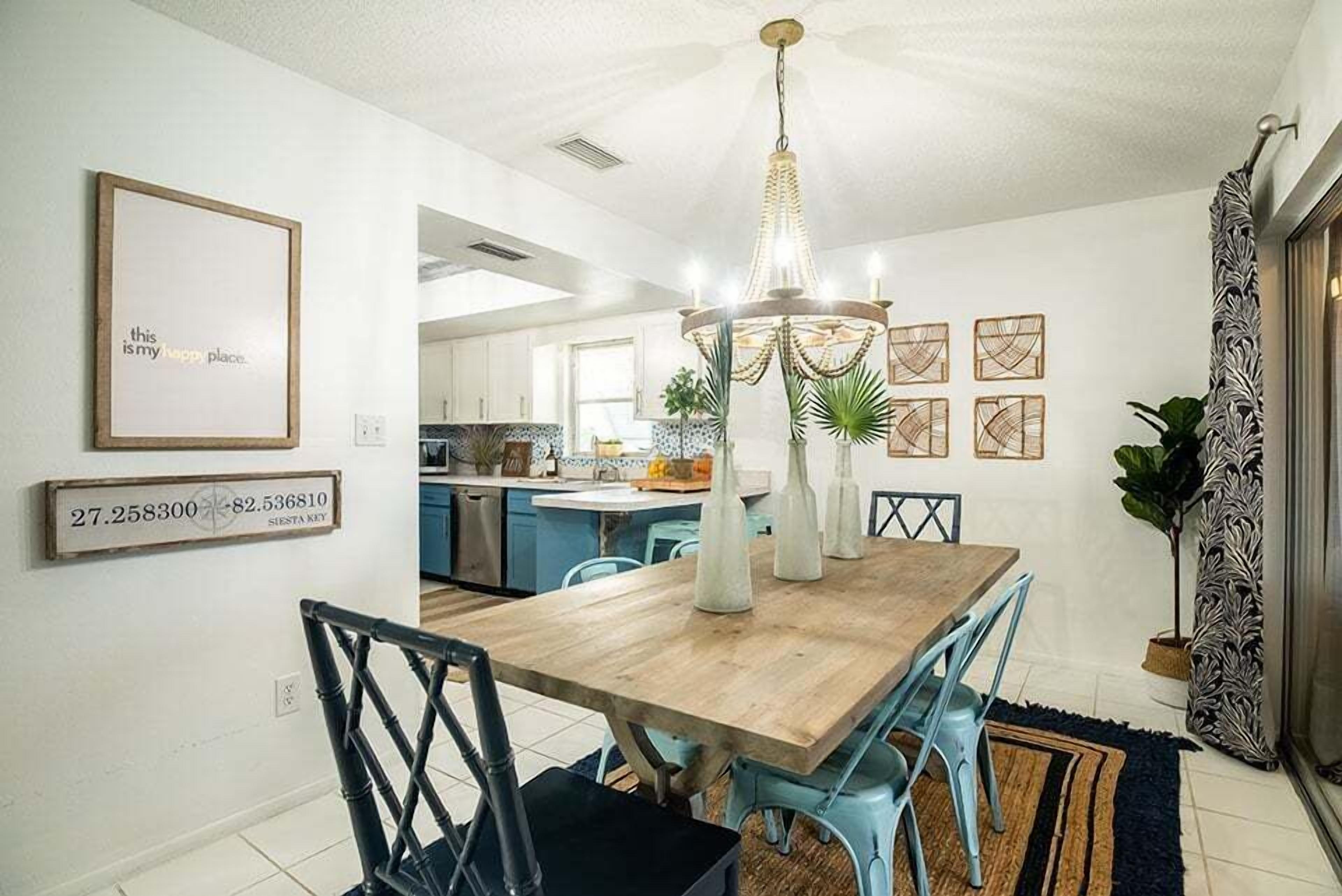 Un coin repas avec une table en bois, des chaises bleues, un lustre et des œuvres d’art encadrées accrochées aux murs.