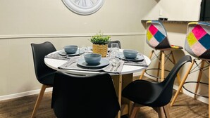 Een eetgedeelte met een ronde tafel gedekt voor vier personen, zwarte stoelen, een klok aan de muur en een kleine potplant.