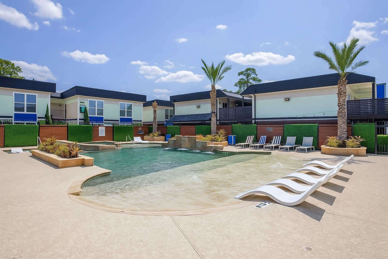 A swimming pool with lounge chairs and palm trees, surrounded by modern buildings with balconies.