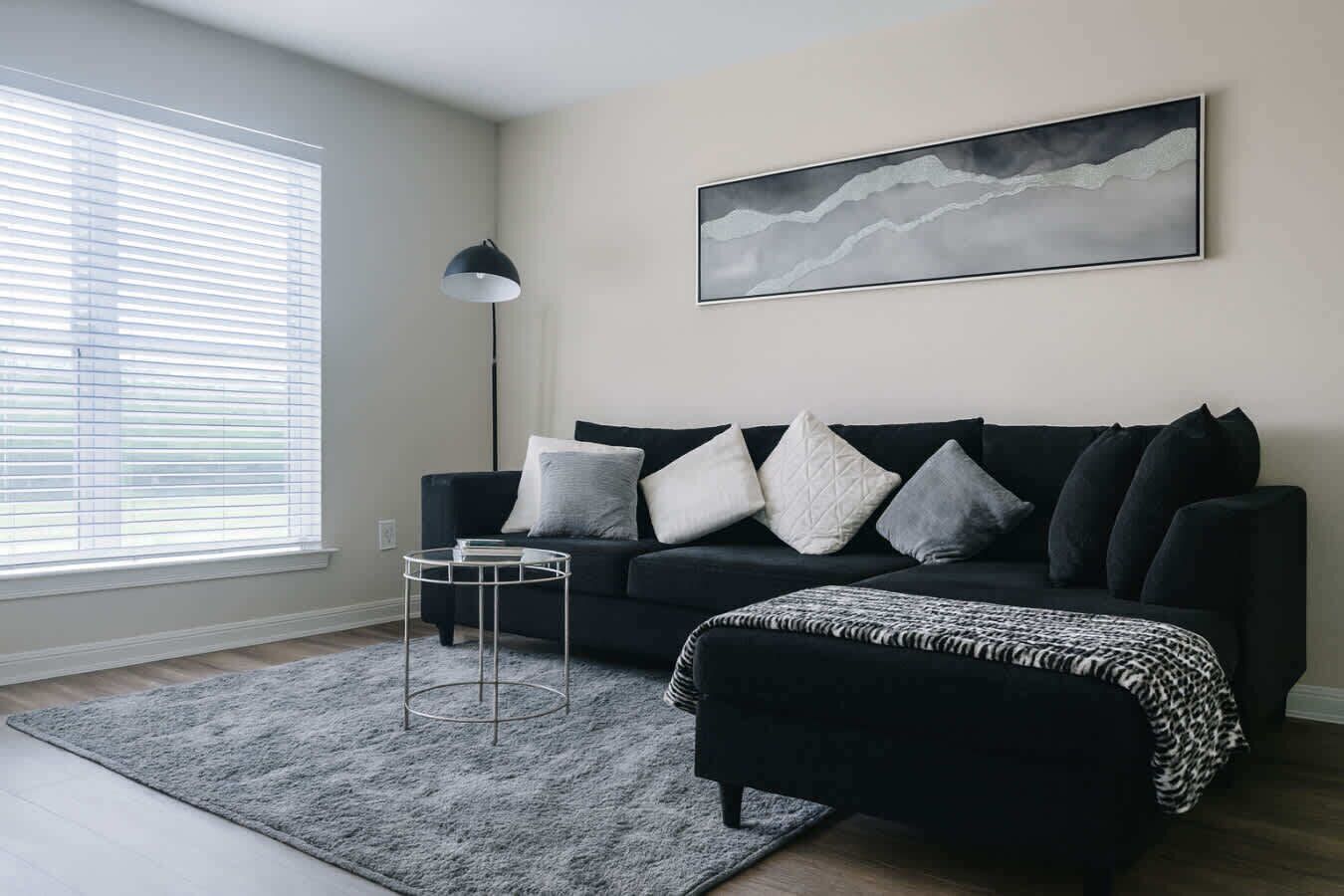 Un salon moderne avec un canapé noir, une table basse ronde, un tapis gris et un lampadaire.