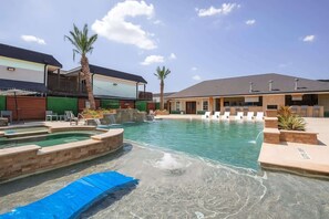 A pool area with lounge chairs, a hot tub, and a building with a flat roof. - King Bed,poolgym BBQ Theheights, Longstaydiscount (Houston)