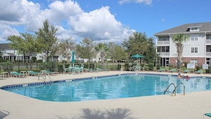 A swimming pool with lounge chairs and a fenced area, surrounded by trees and buildings. - Heatherstone 1063 (Myrtle Beach)