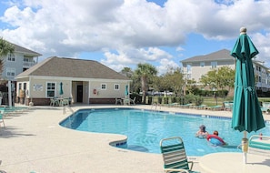 A swimming pool with lounge chairs and umbrellas, surrounded by buildings. - Heatherstone 1063 (Myrtle Beach)
