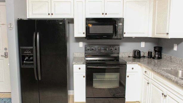 A kitchen with a black refrigerator, a microwave, a stove, and a dishwasher. - Heatherstone 1063 (Myrtle Beach)