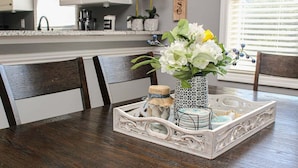 A dining table with a white tray, a vase with flowers, and a small jar with a blue ribbon. - Heatherstone 1063 (Myrtle Beach)