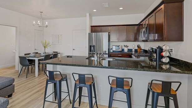 A modern kitchen with a central island, bar stools, and a dining area with a table and chairs. - Bliss Flagstaff 49 (Flagstaff)