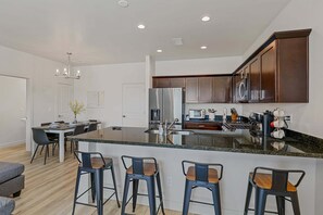 A modern kitchen with a central island, bar stools, and a dining area with a table and chairs. - Bliss Flagstaff 49 (Flagstaff)