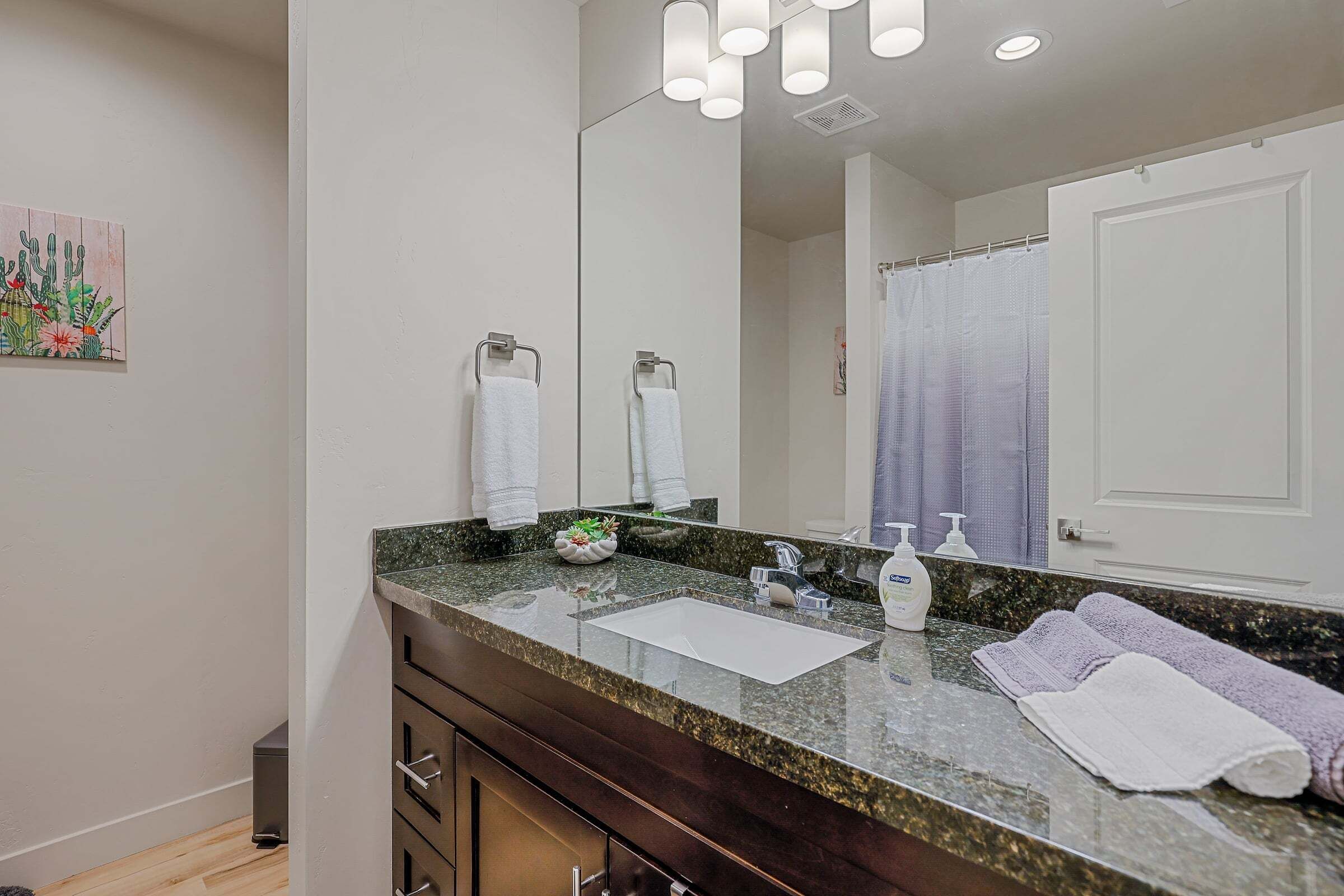 A bathroom with a granite countertop, a white sink, a large mirror, and a shower curtain.