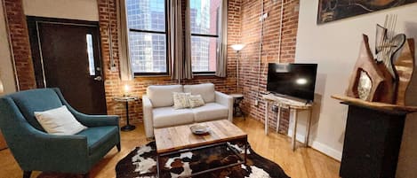 A living room with a brick wall, a sofa, a chair, a TV, and a cowhide rug.