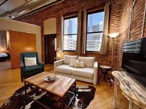 Un salon chaleureux avec un mur en briques, un canapé, un fauteuil, une table basse et un téléviseur.