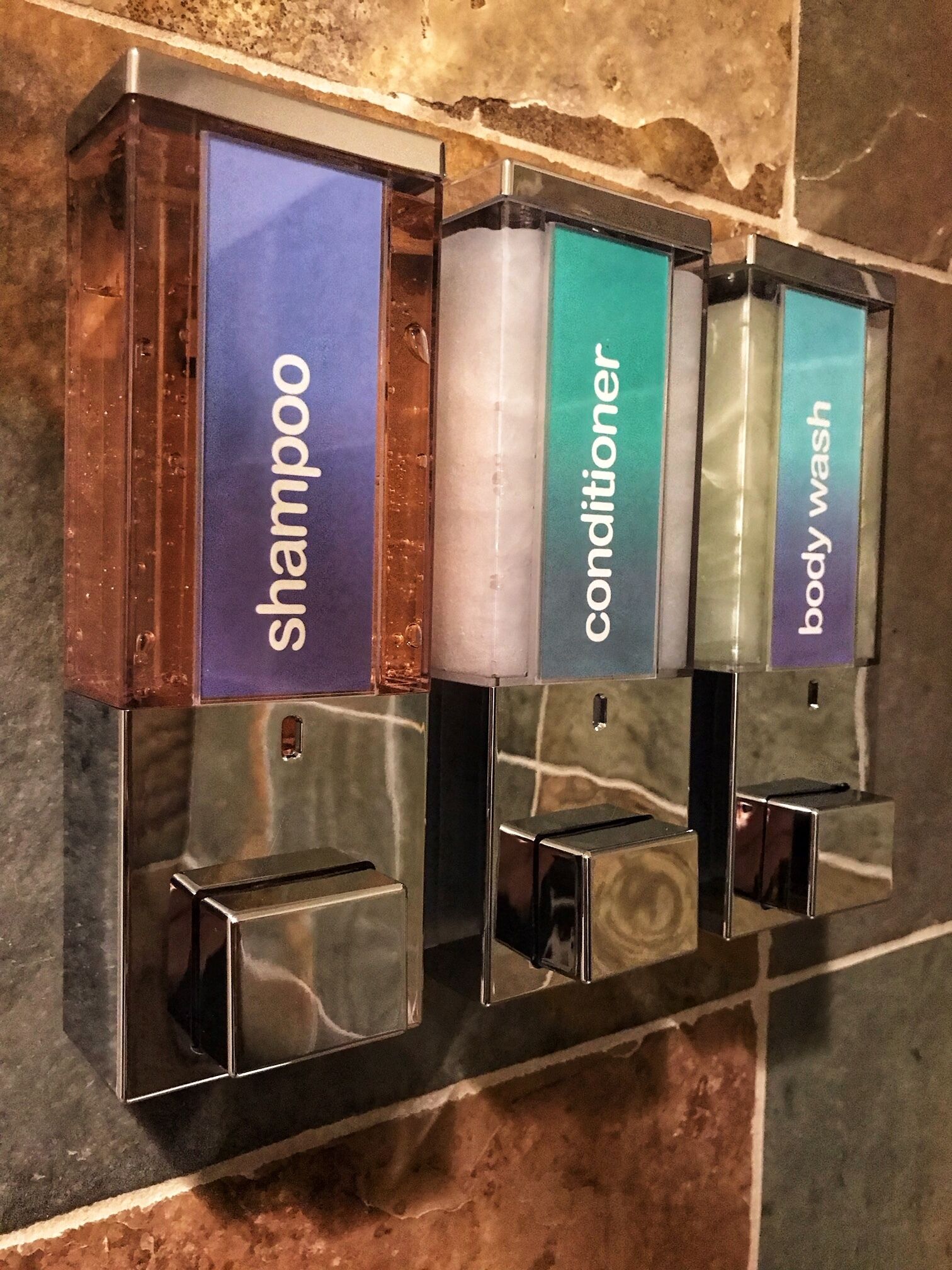 A wall-mounted dispenser with three sections labeled shampoo, conditioner, and body wash.