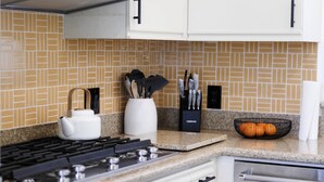 Una cocina con gabinetes blancos, estufa a gas, campana extractora de acero inoxidable y salpicadero de azulejos.