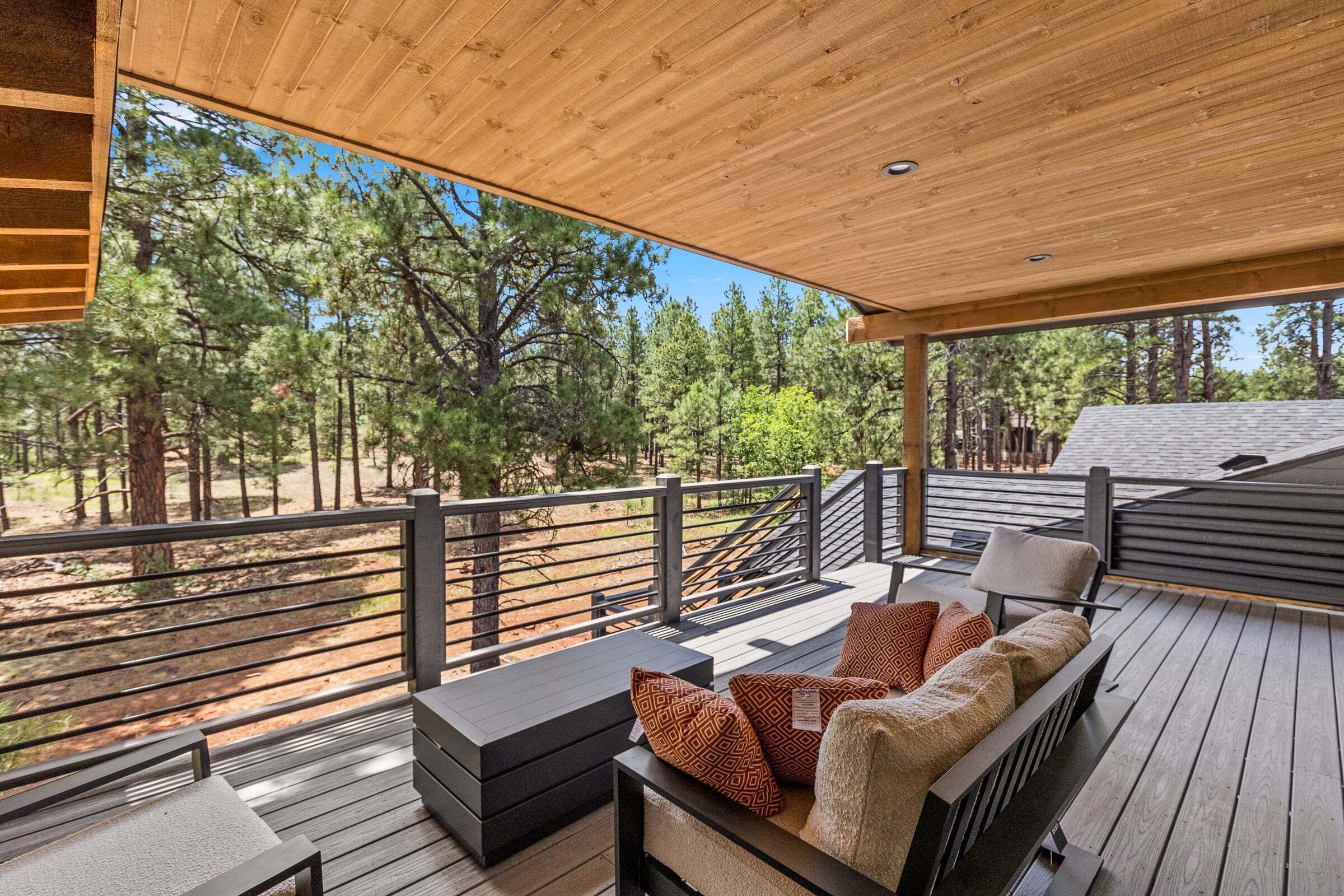 A wooden deck with outdoor seating, a railing, and a view of a forest.