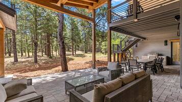 An outdoor patio area with wicker furniture, a glass table, and a barbecue setup.