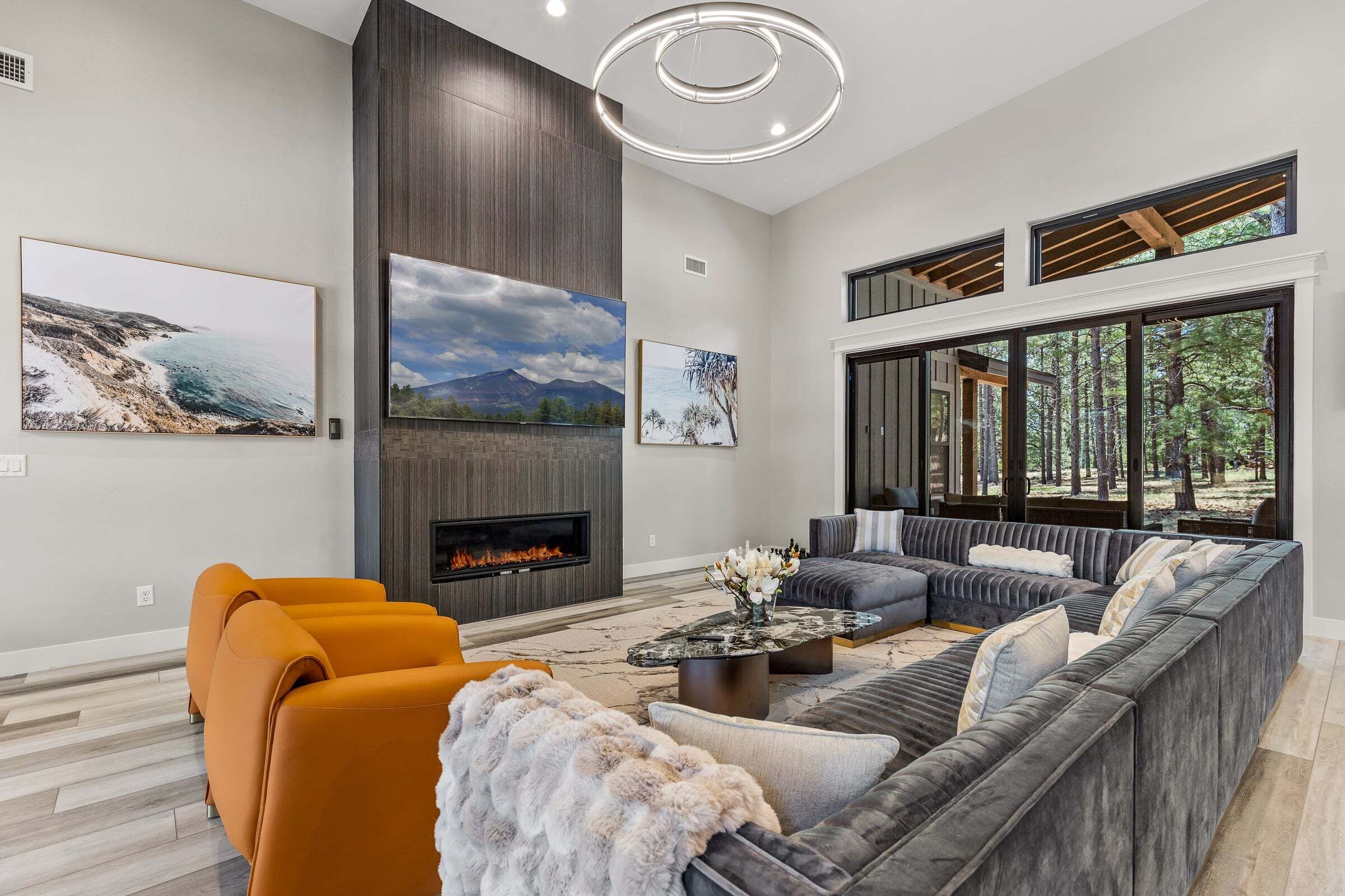 A modern living room with a fireplace, large windows, and artwork on the walls.