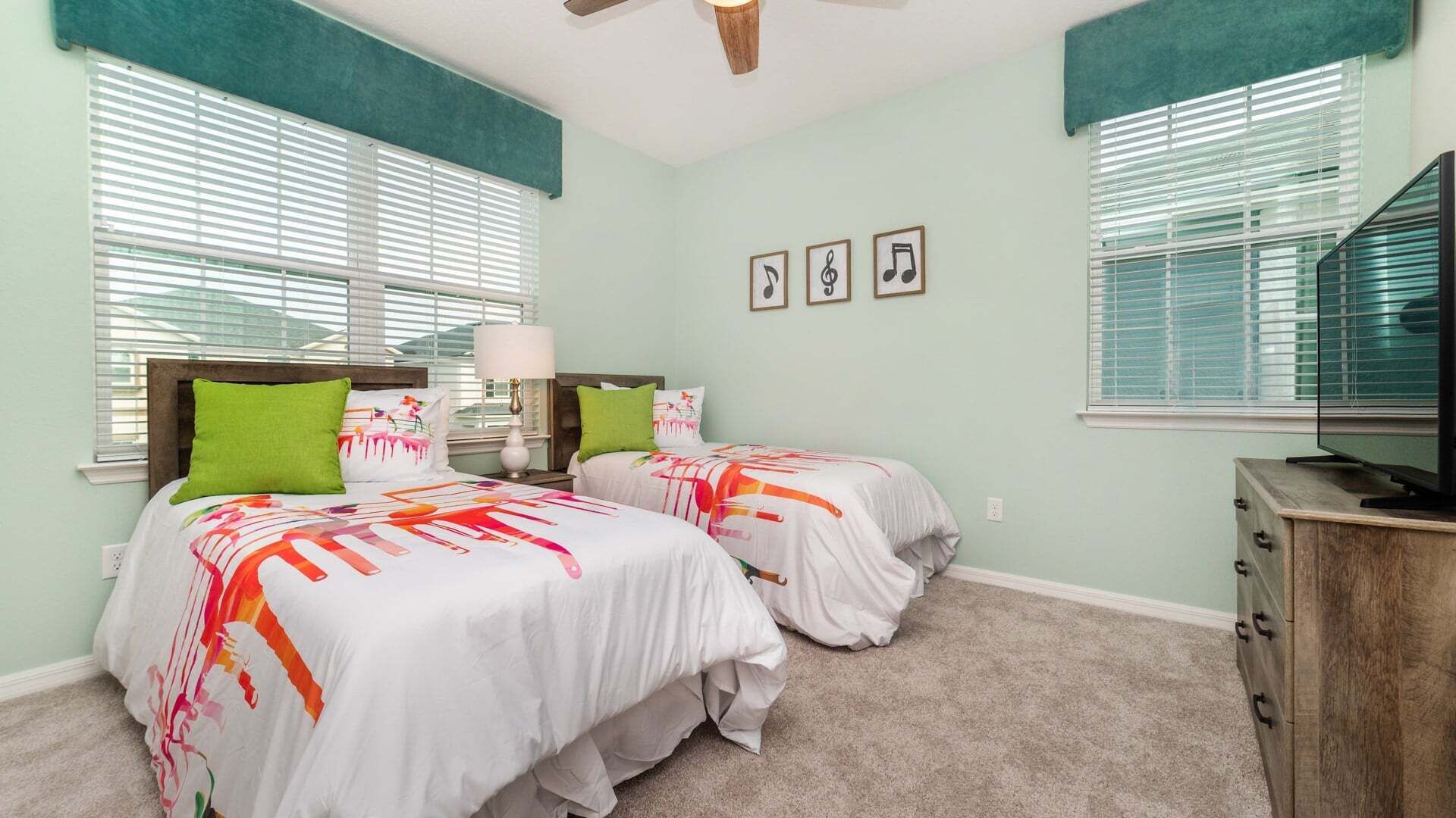 A bedroom with two beds, a ceiling fan, a TV, and a dresser.