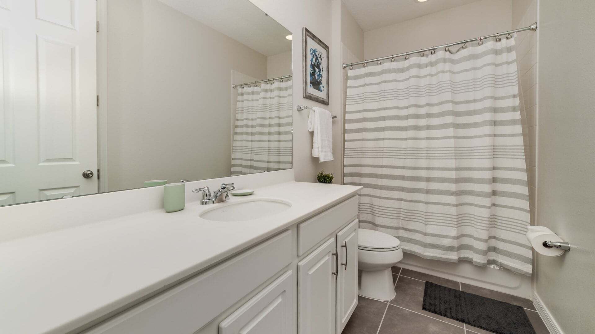 A bathroom with a white sink, a mirror, a toilet, and a shower curtain.