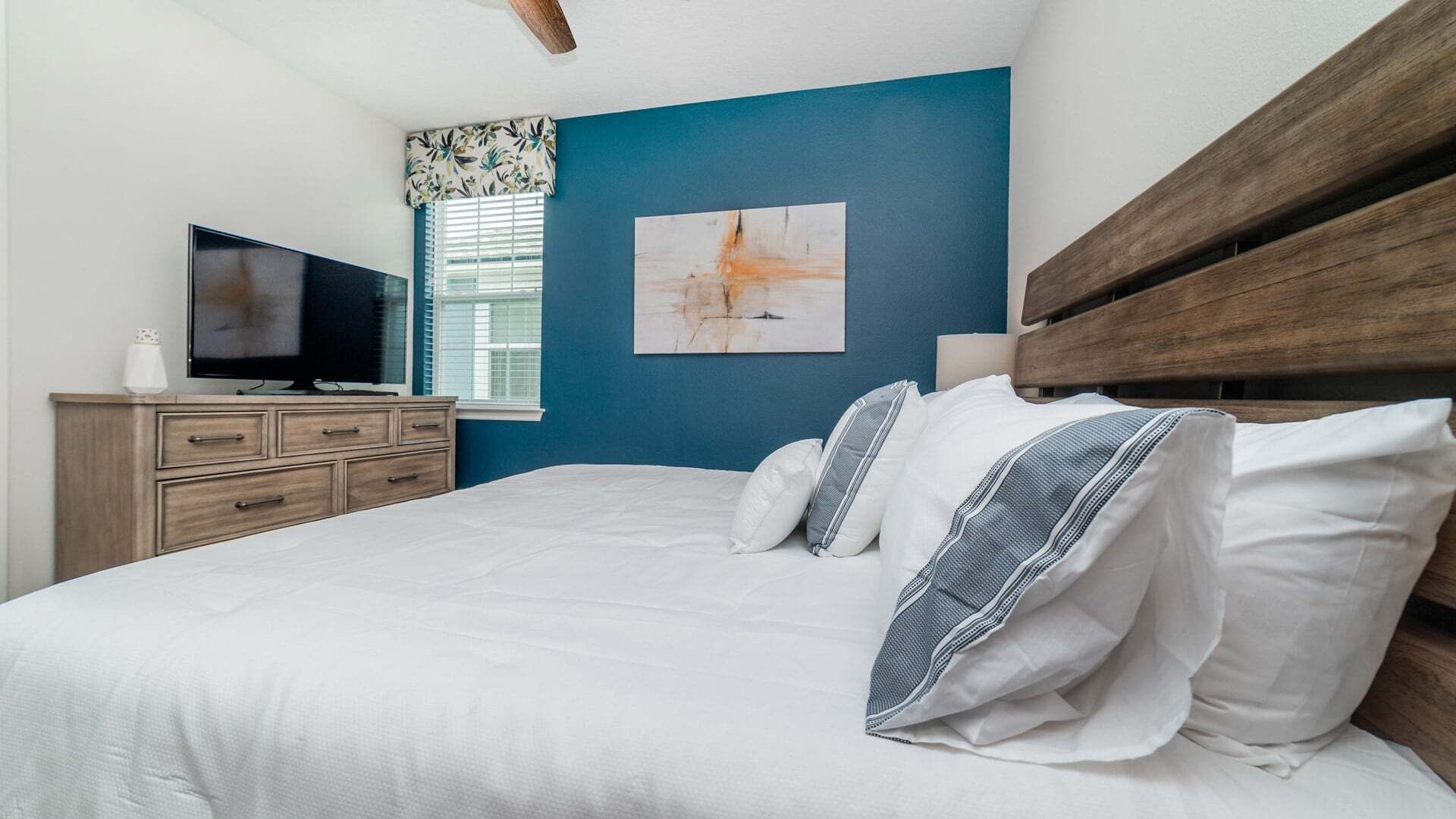 Une chambre à coucher avec un lit, une télévision, une commode et une fenêtre avec des stores.