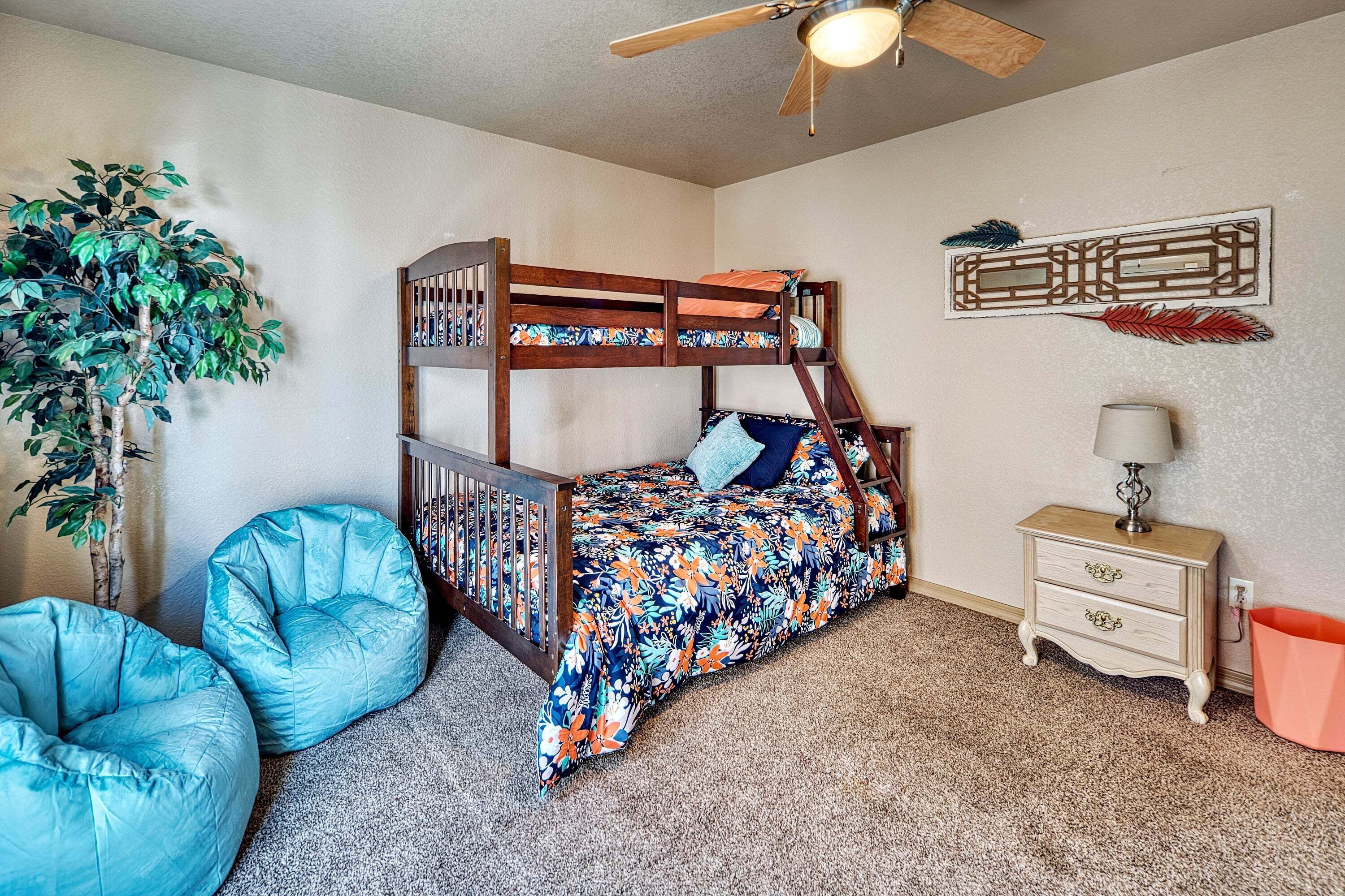 A bunk bed with a floral bedspread, a ceiling fan, a wall-mounted decorative piece, and a potted plant.